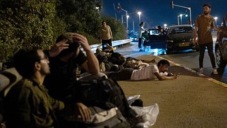 People take cover on the side of a road in the town of Rosh Ha'in, 1 October, 2024 