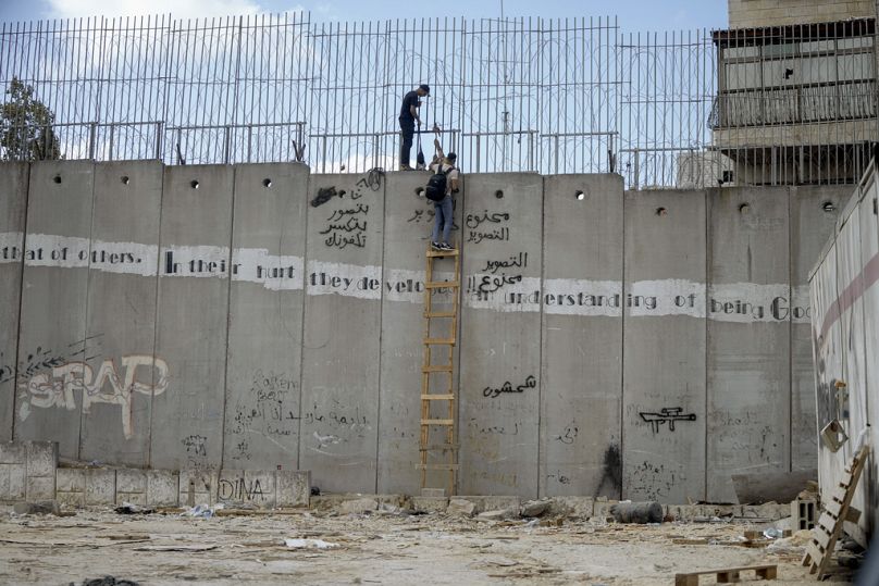 رجال فلسطينيون يتسلقون الجدار العازل في بلدة الرام للعبور بشكل غير قانوني إلى القدس، الأحد، 15 سبتمبر، 2024. 