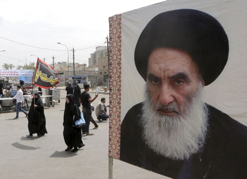 صورة لزوار شيعة يتوجهون نحو ضريح الإمام الكاظم بالعراق وتظهر صورة المرجع علي السيستاني