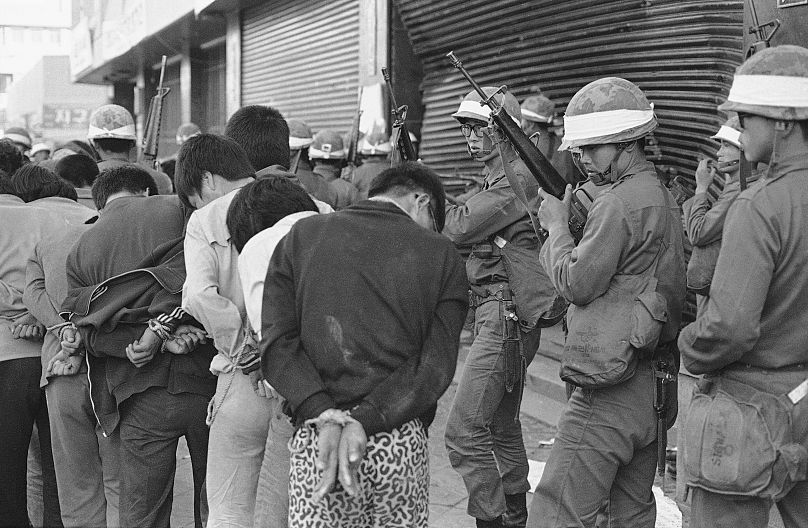 Silahlı Güney Kore hükümet askerleri, 27 Mayıs 1980'de isyanın etkilediği Gwangju (Kwangju) şehrinde ele geçirilen isyancıları bir toplama noktasına götürüyor.