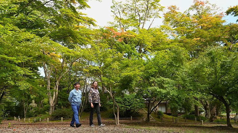 La periodista de Euronews Anca Ulea paseando con el maestro de sake de Asahi-Shuzo, Motoyoshi Yamaga, en el jardín de arces de Momijien