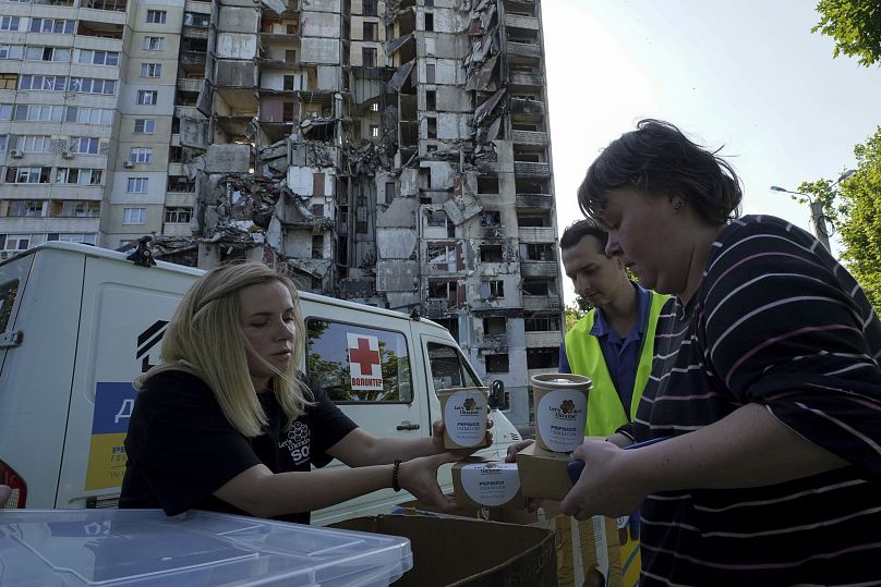 Local residents get free meals from volunteers against the background of their apartment house, damaged in the Russian rocket attack, in Kharkiv, Ukraine, 2 June 2023.