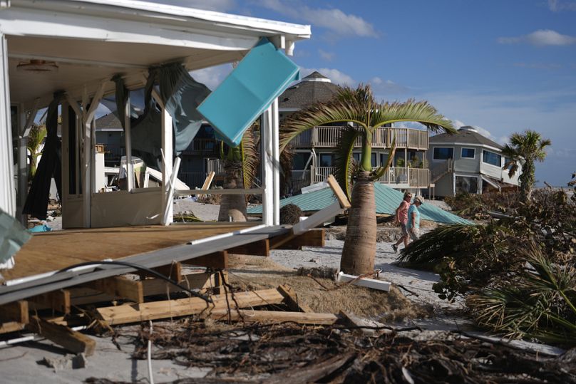 Residents walk past a damaged home and the displaced roof of their 55+ mobile home community's tiki hut after the passage of Hurricane Milton in Englewood, Florida on Sunday