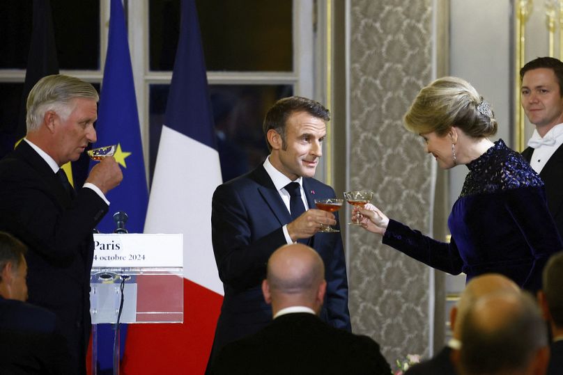 El presidente francés, Emmanuel Macron, en el centro, sostiene una copa para brindar junto al rey Felipe de Bélgica, a la izquierda, y la reina Matilde