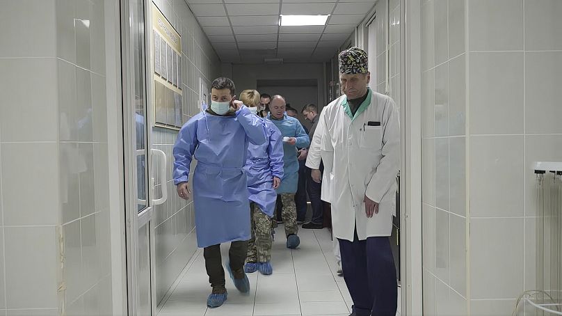Ukrainian President Volodymyr Zelenskyy walks in a surgical gown and mask as he visits doctors, nurses and wounded military members at a hospital in Kyiv, Ukraine.