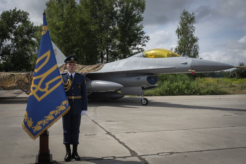 Ein ukrainischer Offizier steht in der Ehrengarde vor dem Hintergrund der F-16-Kampfjets der ukrainischen Luftwaffe an einem ungenannten Ort in der Ukraine, Sonntag, 4. August