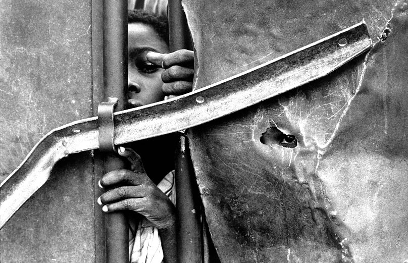Children look through the gates of a feeding center during a famine