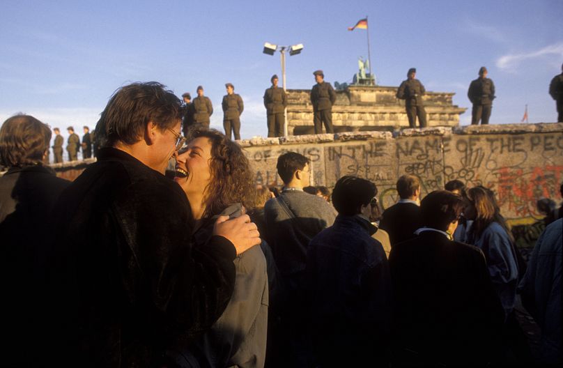 A couple laughs together on the west side of the Berlin Wall as the first people begin crossing into East Berlin in November 1989