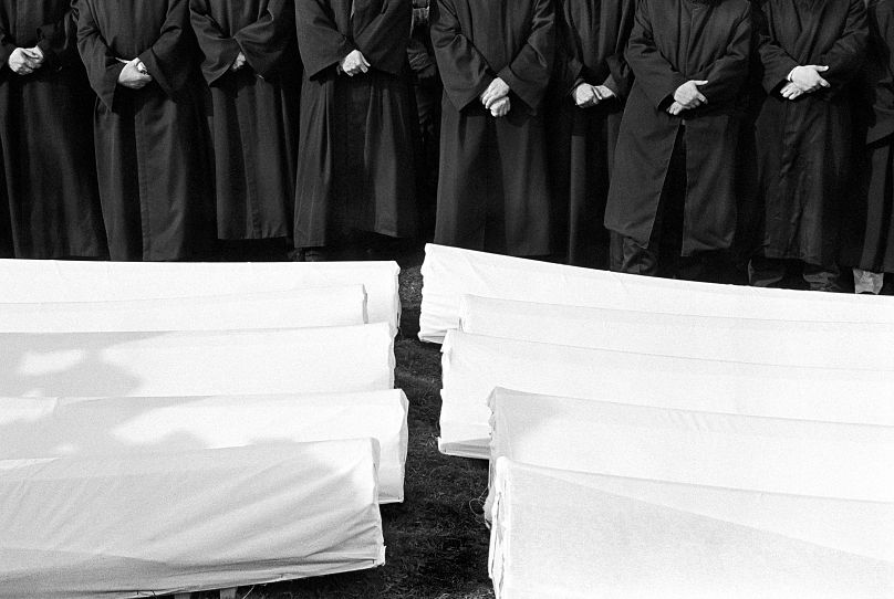 A line of imams pray as the bodies of 40 Muslims are prepared for reburial after being exhumed in 2000.