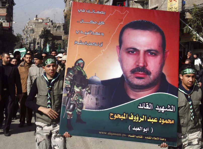 فلسطينيون يحملون صورة محمود المبحوح، أحد مؤسسي الجناح العسكري لحركة حماس، بينما يحمل آخرون نعشه، إلى اليسار، خلال موكب جنازته في مخيم اليرموك للاجئين الفلسطينيين، بالقرب من دم