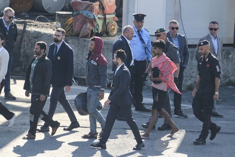 Migrants and security officials walk at the port of Shengjin after disembarking from the Italian navy ship Libra, 16 October, 2024
