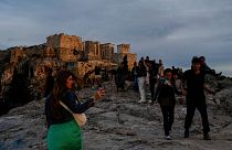 Tourists walk at Areopagus hill in front of the Ancient Acropolis hill as the sun sets in Athens.