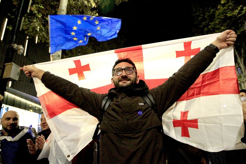 Un uomo con la bandiera georgiana durante una manifestazione dell'opposizione. Sullo sfondo una bandiera dell'Ue, Tbilisi, Georgia, 20 ottobre 2024