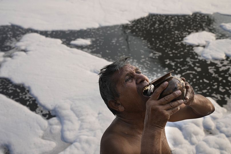 Jasraj, 70, drinks water from the river Yamuna filled with toxic foam in New Delhi, India, Tuesday, Oct. 29, 2024.