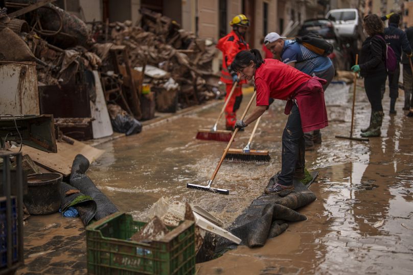 أشخاص ينظفون الطرقات في إحدى المناطق المتضررة من الفيضانات، في ألجميسي، إسبانيا، الأحد 3 نوفمبر 2024. 