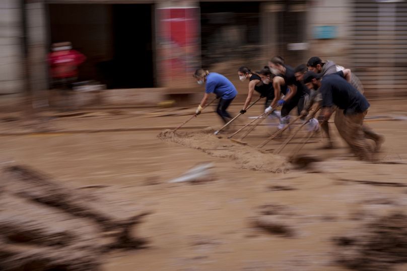 Des personnes enlèvent la boue d'une rue dans une zone touchée par les inondations à Catarroja, en Espagne,
