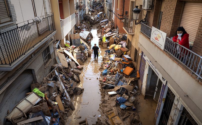 People walk through a street with piled furniture and rubbish on the sides in an area, affected by floods, in Paiporta, Valencia.