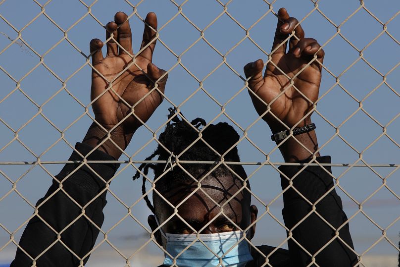 Un migrant portant un masque se tient derrière une clôture à l'intérieur d'un camp de réfugiés à Kokkinotrimithia près de la capitale Nicosie, Chypre, vendredi 5 février 2024