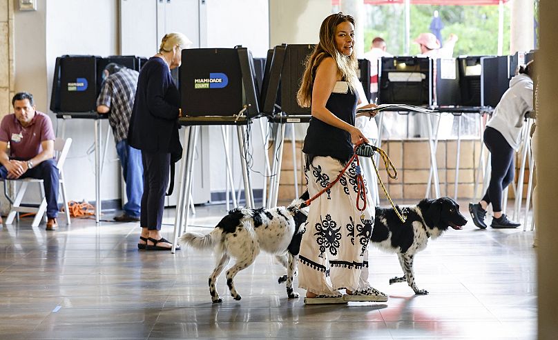 Eva Moore transporta o seu boletim de voto com os seus cães de serviço Apollo e Vinkenoog no Coral Gables Country Club, na Florida. 5 de novembro de 2024.