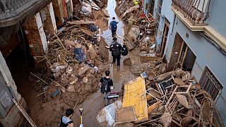 People walk through a street with piled furniture and rubbish on the sides in an area, affected by floods, in Paiporta, Valencia, Spain.