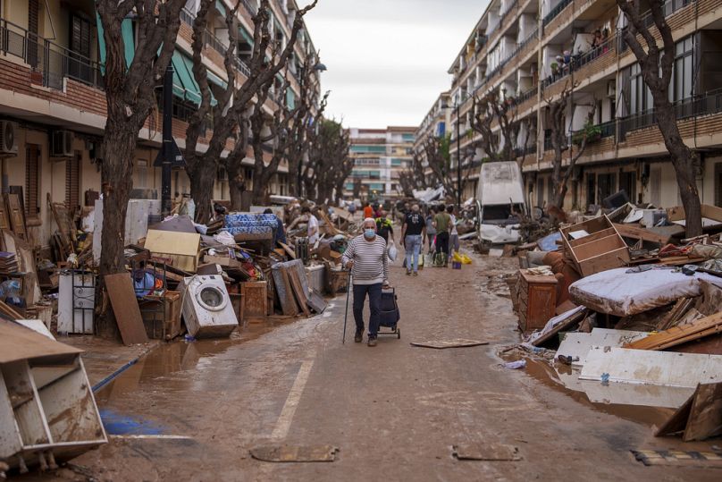Des personnes marchent dans une rue où des meubles et des déchets sont entassés sur les côtés, dans une zone touchée par les inondations à Benetusser. le 4 nov 2024.