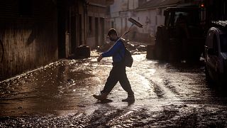 A volunteer walks with a broom over a muddy street in Massanassa, Valencia, Spain.