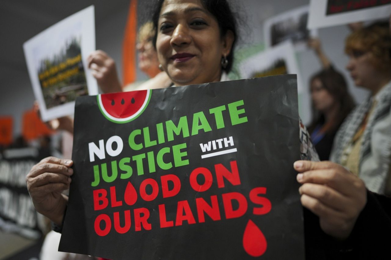 An activist holds a sign that reads "no climate justice with blood on our lands".