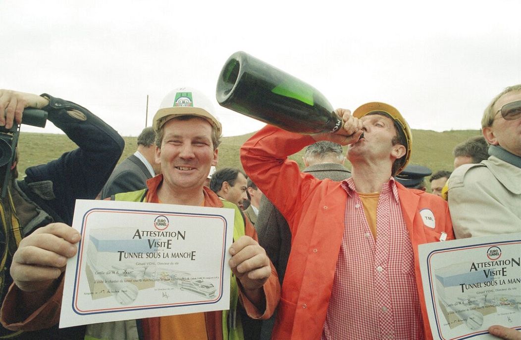 Lead miner Roy West presents his visitor certificate as shift boss Ray Green drinks Champagne to celebrate the breakthrough of the Channel Tunnel - Sangette, France. Dec 1990