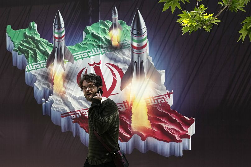 A passerby walks past a banner showing missiles being launched from an Iranian map in Tehran, 19 April, 2024