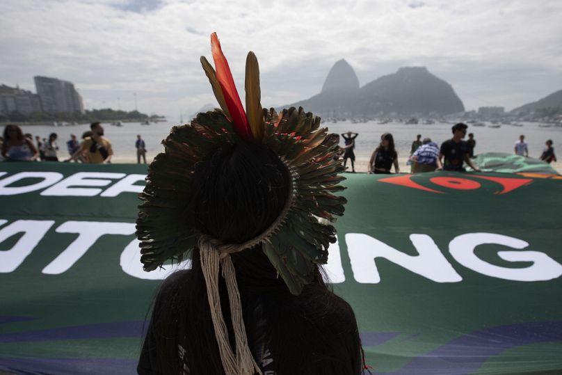 Txai Surui, a Paiter-Surui indigenous woman, and activists from the Amazônia de Pé movement hold a banner that reads: "World Leaders: The Amazon is watching."