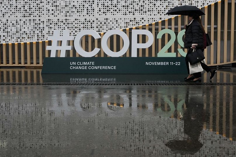 Des personnes arrivent sous la pluie au sommet climatique COP29 de l'ONU, le lundi 18 novembre 2024, à Bakou, en Azerbaïdjan.