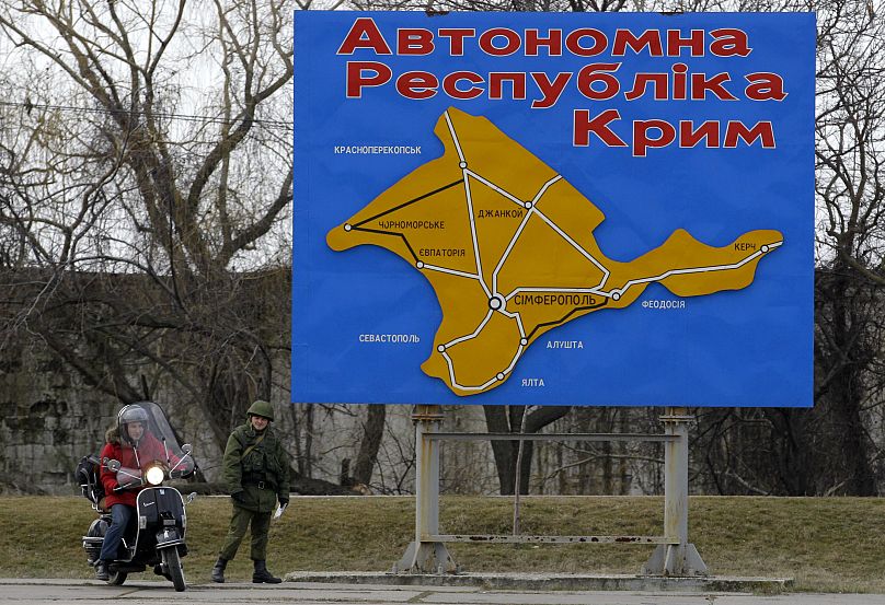 A pro-Russian soldier stands by a billboard with a map of Crimea and bearing the words "Autonomous Republic of Crimea" in the port of Kerch, Ukraine, Monday, March 3, 2014