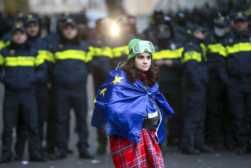 Une femme tient un drapeau de l'UE devant la police qui bloque l'entrée du bâtiment du Parlement lors d'un rassemblement pour demander de nouvelles élections parlementaires.