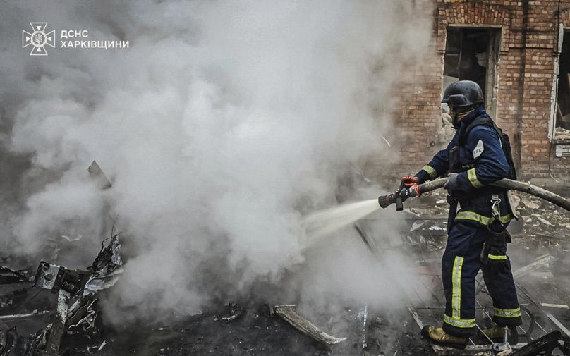 Un pompier éteint le feu d'une voiture brûlée dans la cour d'un immeuble d'habitation endommagé par une frappe russe à Kharkiv