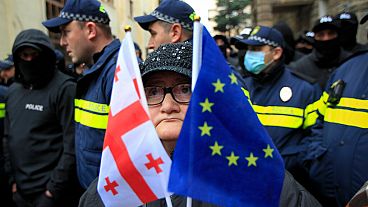 Eine Frau mit einer EU- und einer georgischen Nationalflagge steht vor der Polizei in der Nähe des Parlamentsgebäudes in Tiflis, Georgien, am Montag, 25. November 2024.