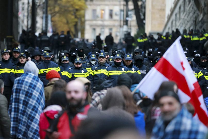 Protesters with a Georgian national flag stand in front of police blocking the entrance of the Parliament's building in Tbilisi, Georgia, Monday, Nov. 25, 2024. 