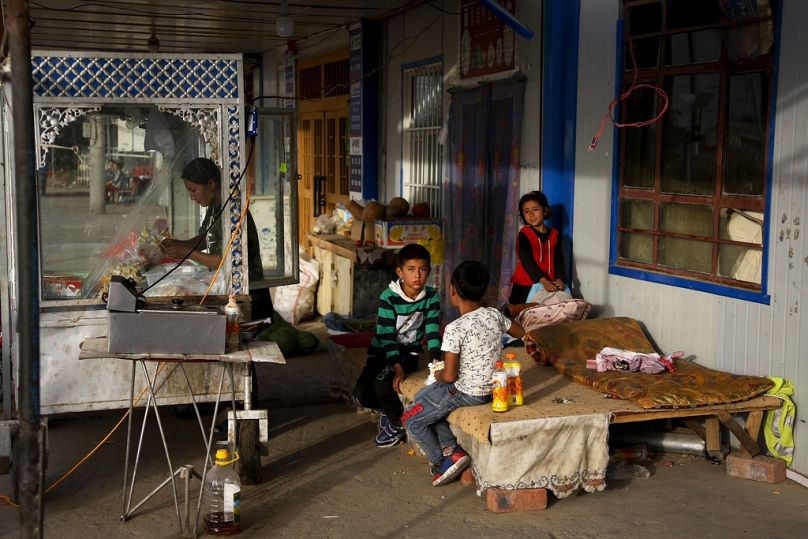 A Uyghur woman works at her food stand while her children play in a resting place nearby at the Unity New Village in Hotan, in western China's Xinjiang region, September 2018