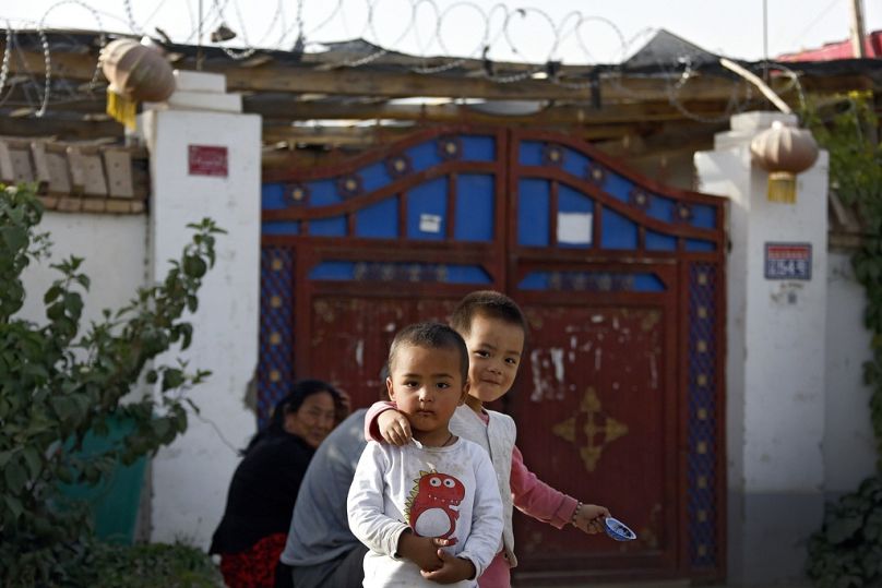 Uyghur children play while their relatives rest outside their house, decorated with lanterns and barbed wire at the Unity New Village in Hotan, September 2018