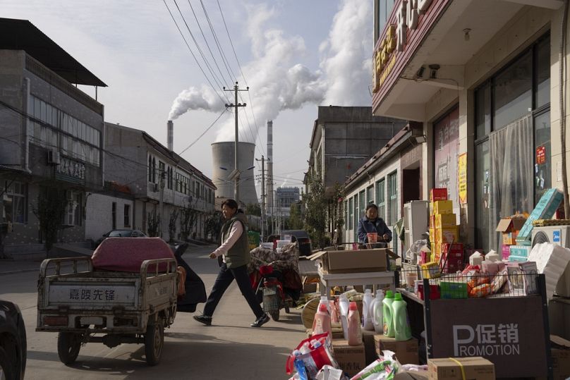 Guohua Power Station, a coal-fired power plant, operates as people sell items on a street in Dingzhou, Baoding, in the northern China.