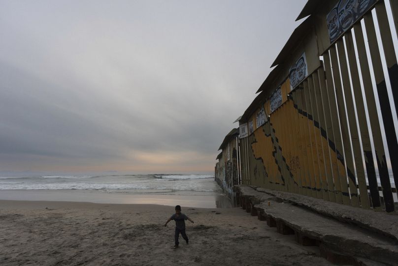 Un bambino cammina vicino al punto in cui il muro di confine che separa gli Stati Uniti dal Messico raggiunge l'Oceano Pacifico, 26 novembre 2024, Tijuana, Messico
