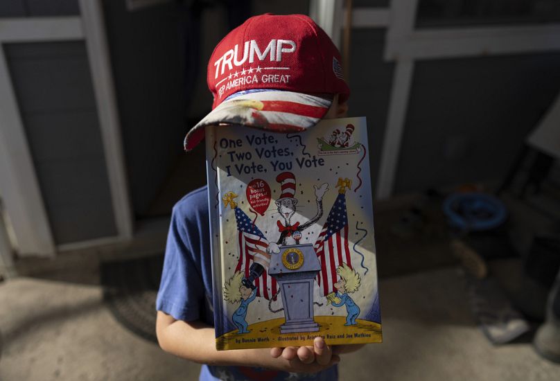 A five-year-old wears his "Trump Keep America Great" hat as he holds up the book, "One Vote, Two Votes, I Vote, You Vote", in Sunbury, OH, November 2024