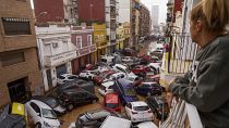 A woman looks out from her balcony as vehicles are trapped in the street during flooding in Valencia