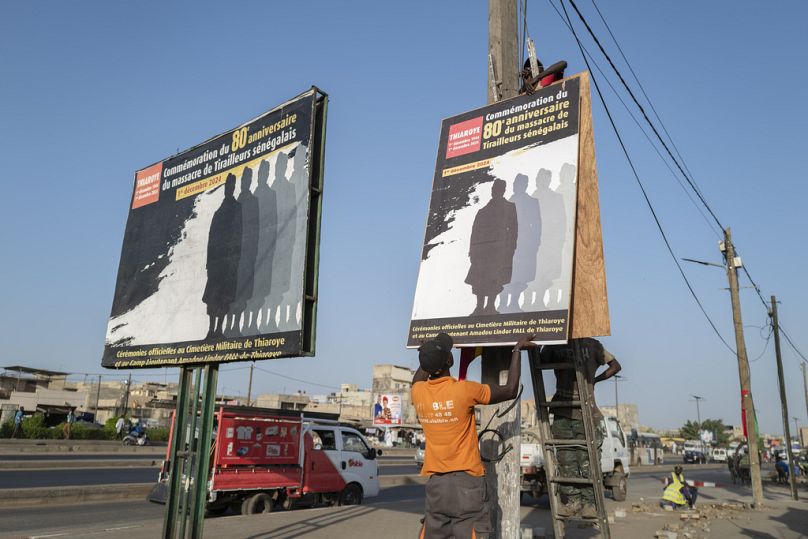 عمال يضعون ملصقًا بمناسبة الذكرى الثمانين لمجزرة ثياروي ثياروي، المسؤولة عنها فرنسا في السنغال، الخميس، 28 نوفمبر/تشرين الثاني 2024. 