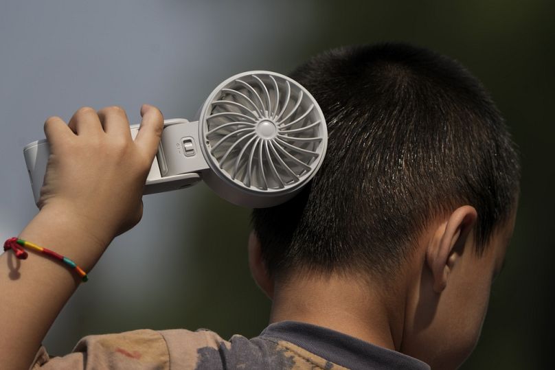 A boy cools himself with an electric fan on a sweltering day at a park in Tongzhou, on the outskirts of Beijing, June 2024