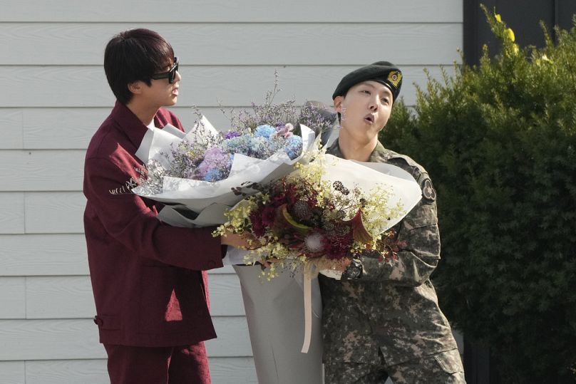 BTS-Mitglied Jin (links) holt seinen Bandkollegen J-Hope (rechts) vom Militärdienst mit Blumen ab..