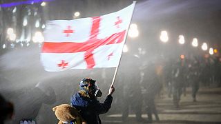 Manifestante tiene una bandiera nazionale georgiana mentre viene spruzzato da un cannone ad acqua fuori dal Parlamento durante una protesta, a Tbilisi, in Georgia, 3/12/2024