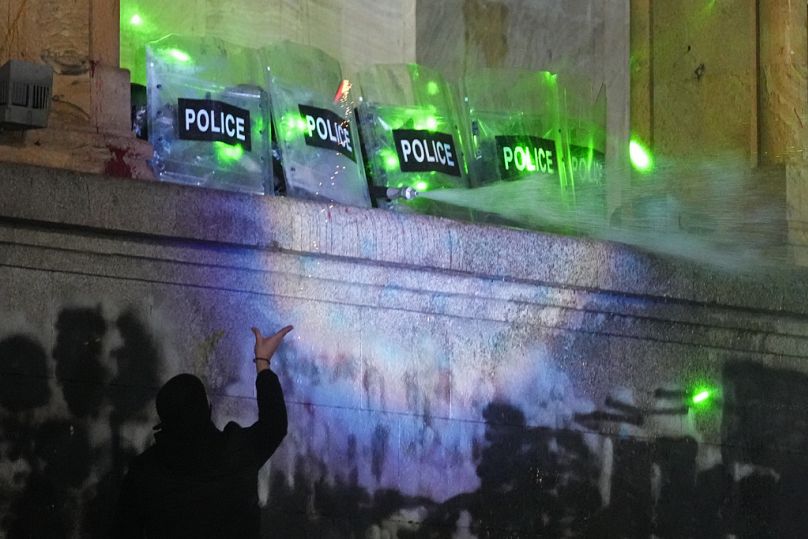Demonstranci stoją pod bieżącą wodą z pompy strażackiej używanej przez policję podczas wiecu przed parlamentem w Tbilisi w Gruzji we wtorek, 3 grudnia 2024 r.