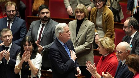 French Prime Minister Michel Barnier gets applause from ministers and parliament members after addressing the National Assembly prior to a vote on a no-confidence, 2024. 