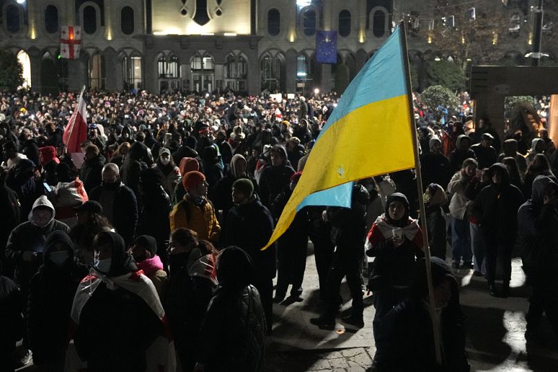 Des manifestants protestent contre le gouvernement à Tbilissi, en Géorgie, le mardi 3 décembre 2024, l'un d'entre eux tenant un drapeau national ukrainien. 