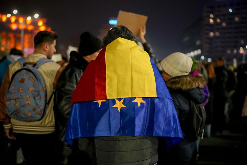Un uomo con le bandiere della Romania e dell'Unione Europea sulle spalle partecipa a una protesta contro Calin Georgescu, Bucarest, Romania, 27 novembre 2024